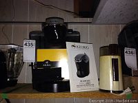 Keurig coffee maker alongside coffee grinder and the Keurig use and care manual on a shelf.