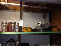 Overall shot showing two yellow Le Creuset pots, Mason jars, and various bakeware stacked on green shelf.
