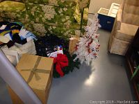 Photo of white small Christmas tree decorated with red bead garland and silver bells, coiled Christmas lights, green garland and cardboard box in a room with green floral couch and beige chair.