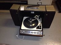 Photo showing the RCA Victor portable turntable unit with the lid open, revealing the record player and two integrated cloth-covered speakers on either side.