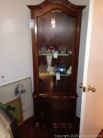 Full view of the tall wood framed curio display cabinet with glass door and shelves, contents removed. Shows curved crown molding and lower wooden door storage compartment.