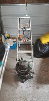 Overall view of 5ft aluminum ladder with shop vac in front and other items visible around.
