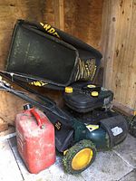 Green Craftsman 3 In 1 lawnmower with attached black and yellow grass collection bag next to red fuel container. Shows front and side view with yellow wheels and some grass residue.