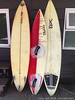 Three surfboards propped against wall, showing full fronts