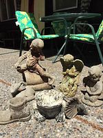 Overview of the lawn ornaments including the boy figurine, angel, cherub, frog, bird, boot planter, deer, and shell shapes on a patio surface under daylight.