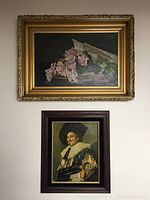 Two framed artworks on wall, larger painting with gold ornate frame depicting pink flowers and smaller framed print below with portrait of man in historical attire