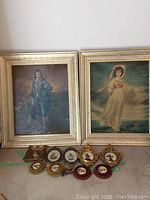 Two large framed prints with several small framed miniature portraits in front laid out on floor