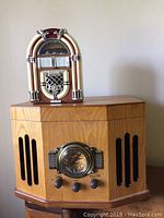 Front view of wooden cabinet AM-FM radio with black grill slits and small decorative jukebox on top.