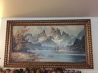 Full view of large landscape painting with three mountain peaks, lake, trees, and golden ornate frame.