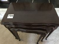 Set of three wood nesting tables stacked together showing curved edges and smooth wood finish.