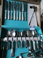 Flatware set inside an open Oneida chest showing knives, forks, spoons, and a ladle arranged in designated slots.