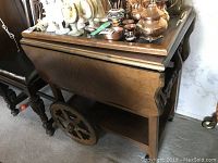 Side view of wooden bar cart showing drop leaf side and large carved wooden wheel