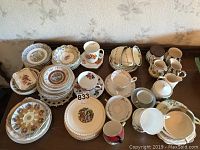 Overview of multiple stacks of assorted tea cups, saucers, plates, and dishes in handpainted porcelain with various floral and classical designs