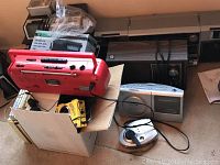Overview of lot contents including red cassette player, small radios, portable CD player, and boxed Tamco 10-band radio