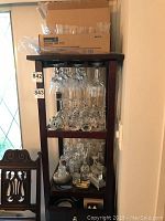 Full view of a dark wooden shelving unit filled with various glassware including wine glasses, tumblers, vases, and decorative glass items.