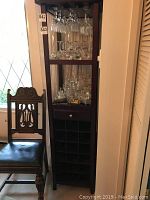 Full view of the wine rack and glass unit next to a wooden chair showing height and overall construction.