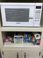 Panasonic white inverter microwave on top shelf with assorted paper and plastic kitchen supplies below