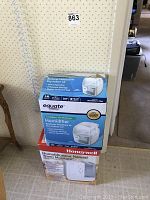 Two humidifiers in original boxes stacked vertically against a wall, Honeywell at bottom and Equate at top