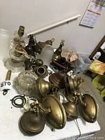 Various vintage lamps and parts laid out on a table including brass wall sconces, glass lampshades, and metal fixtures.
