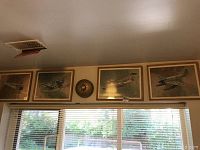 Four framed military aircraft art prints displayed above a window, each print depicts different aircraft with wooden frames