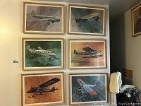 Full view of six framed vintage airplane prints on a wall, arranged in two rows of three. Each print shows a different airplane in varying flight settings and color backgrounds, framed in simple wood frames.