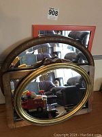 Four mirrors displayed on the floor and leaned against a wall showing different frame styles and sizes
