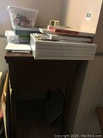 Photo showing wooden square artist table with several blank canvases and plastic bins stacked on top.