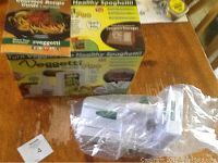 Picture of Veggetti Pro box, instruction booklet, and spiral cutter wrapped in plastic showing the new condition and contents.