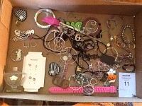 Full box view showing assorted costume jewelry including necklaces, bracelets, pendants, earrings, pink wristwatch, and perfume bottle.