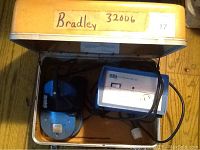 Open metal case showing EBI BiOsteogen System 204 controller and blue headset inside with cables, resting on foam lining.