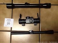 Three rifle scopes displayed on a tile floor: a short scope with adjustment knobs and mounting brackets in the center, one longer tubular scope above it, and another long scope below. This shows the full set and physical size of each scope.