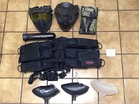 Photo shows two paintball masks, two pod carriers, nine paintball pods, and three hoppers laid out on floor tiles.