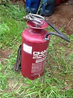 Photo of red Chapin sprayer tank with hose and spray wand placed on grass outdoors