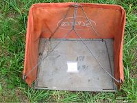 Top-down view of the orange fabric grass catcher with metal wire frame and metal base plate, showing the Scotts logo on the fabric and attachment frame.