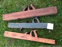 Three large wooden hand planes arranged on grass showing different finishes and wood handles.