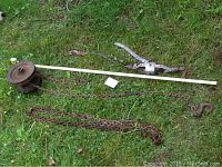 Old Triplex quarter ton pulley hoist with metal chains and a tape measure for scale on grass.