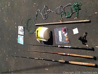 Full set of fishing rods along with net, stringer, bait container, bobbers and reel laid out on ground
