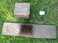 Full view of the antique wool carding board with spikes and the separate protective wooden cover placed on grass.