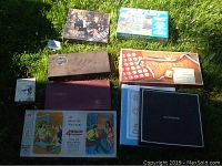 Full overview showing all games and photo albums arranged on grass, displaying Scrabble box, photo albums, puzzles, and Presidents set.