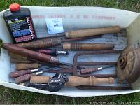Overview photo of various old wooden-handled tools including chisels and screwdrivers, a metal pitchfork head, and a black bottle of radiator additive in a white container