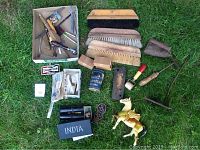 Photo of assorted brushes, knives, vintage iron, tools, patches, and small collectibles arranged on grass.
