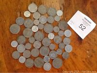 Top view of 43 foreign coins spread out on a wooden surface with visible numeric denominations and various designs.