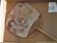 Photo of the top side of a round paper fan with wooden ribs, showing Rubifoam logo and colorful illustrations of roosters and a man holding a brush.