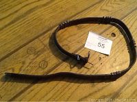 Full view of the coiled leather belt strap on wooden floor showing entire length and metal rings