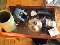 Box with two black hole punches, sheath, and miscellaneous small items including plastic packaging and a spherical object.