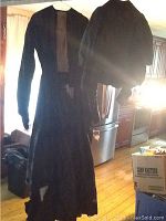 Long black Victorian style women's dress hanging on white hanger, showing full length and fabric.