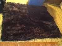 Top view showing the entire black fur blanket or rug laid flat on wooden floor.