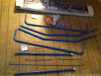 Full lot of blue tubular metal frame pieces laid out on wood floor, plus packaging box.