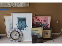Five framed pieces of wall art and one round alarm clock, all leaning against the wall on carpeted floor.
