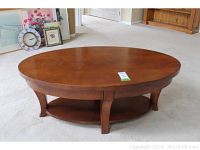 Full view of the solid wood oval coffee table showing its shape, legs, and lower shelf.